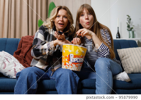 Mother and daughter are concentrating on watching an interesting movie and eating popcorn while sitting on the couch 95879990