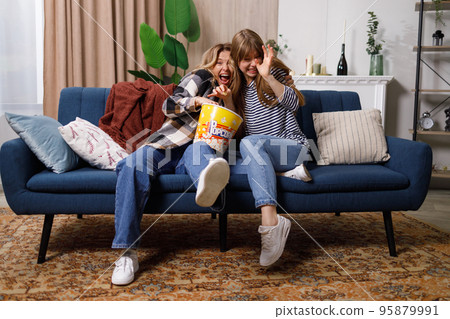 Frightened women watching horror movie and eating popcorn at home 95879991
