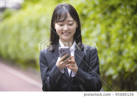 A young woman looking at her smartphone in a recruit suit 95880126
