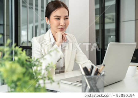Asian businesswoman uses a laptop to analyze a company's financial business graph, Using a laptop for telecommunication work, Happy woman working in front of laptop screen, Modern private office room 95880194