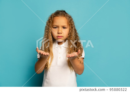Resentment. Sad little girl, kid with long hair wearing white t-shirt expressing emotions isolated over blue background. Concept of children emotions, fashion, beauty, back to school and ad Resentment. Sad little girl, kid with long hair wearing white t-shirt expressing emotions isolated over blue background. Concept of children emotions, fashion, beauty, back to school and ad 95880322