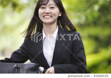 A young woman pulling a bicycle in a recruit suit A young woman pulling a bicycle in a recruit suit 95880430
