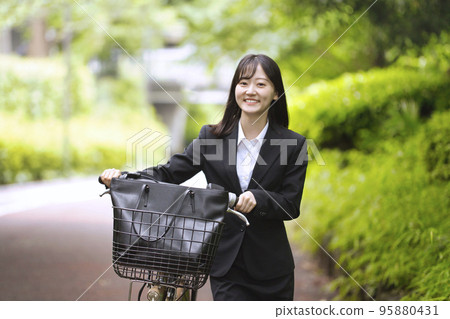 A young woman pulling a bicycle in a recruit suit A young woman pulling a bicycle in a recruit suit 95880431