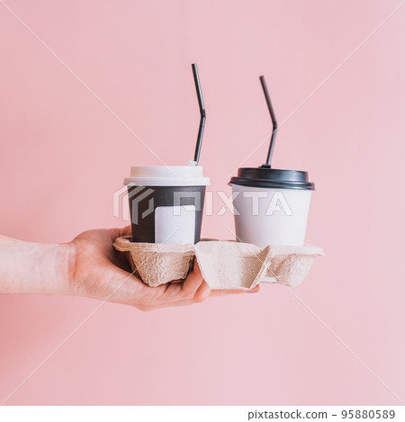 Coffee to go with straws on trays in hand against pink background Coffee to go with straws on trays in hand against pink background 95880589