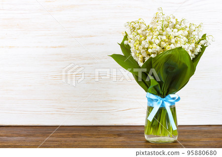 bouquet of lilies of the valley in a vase with blue ribbon on a brown white wooden background bouquet of lilies of the valley in a vase with blue ribbon on a brown white wooden background 95880680