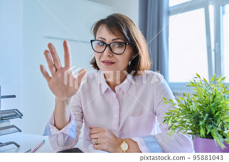 Webcam view of talking mature woman sitting at desk in home office Webcam view of talking mature woman sitting at desk in home office 95881043