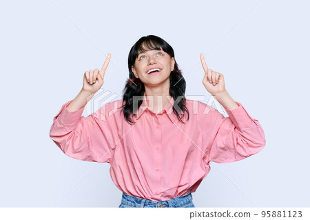 Young woman pointing fingers up, space for copyspace text, on light background Young woman pointing fingers up, space for copyspace text, on light background 95881123
