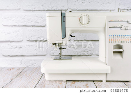 Modern sewing machine on white brick background Modern sewing machine on white brick background 95881478