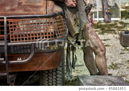 Completely rusted front part of suv with grills in front of headlight and dirty bare legs in background 95881951