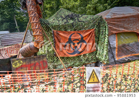 Tent with a camouflage net and a loge with the warning of a biohazard in a tent camp after the destruction of the world Tent with a camouflage net and a loge with the warning of a biohazard in a tent camp after the destruction of the world 95881953