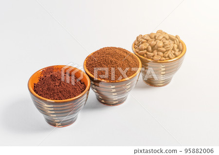 three small saucers with coffee beans, ground coffee and cocoa on a white background. 95882006