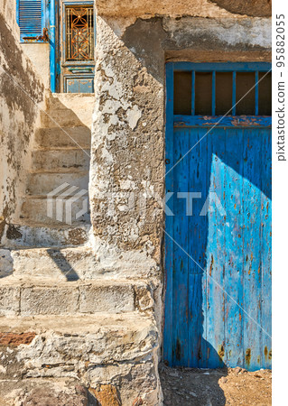 Faded and weathered white wall and stairs, blue painted door, Greece. Traditional architecture, details, authentic facade, sunny day, sunshine, shadow Faded and weathered white wall and stairs, blue painted door, Greece. Traditional architecture, details, authentic facade, sunny day, sunshine, shadow 95882055