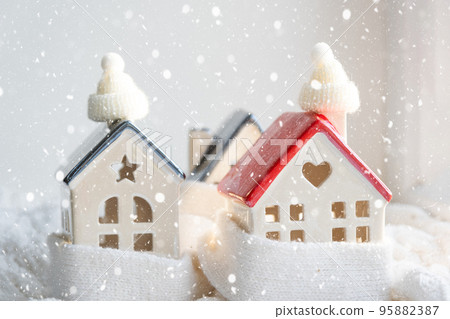 Cozy house is wrapped in a hat and scarf in a snowstorm -window sill decor. Winter, snow - home insulation, protection from cold and bad weather, room heating system. Festive mood, Christmas, New Year 95882387