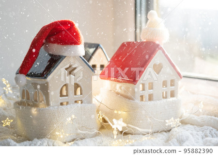 Cozy house is wrapped in a hat and scarf in a snowstorm -window sill decor. Winter, snow - home insulation, protection from cold and bad weather, room heating system. Festive mood, Christmas, New Year 95882390