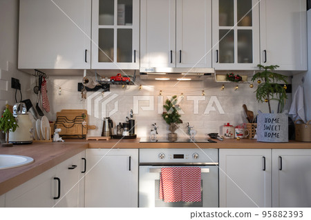 Christmas kitchen decor - preparation for a family holiday, fairy light, Christmas tree, red ornament, funny deer on cabinets, stove. Mood of celebration, eve, New year 95882393