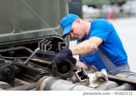 Mechanic in overalls repairs truck on summer day outside. Urgent repair of trucks. Authentic Mechanic in overalls repairs truck on summer day outside. Urgent repair of trucks. Authentic 95882512