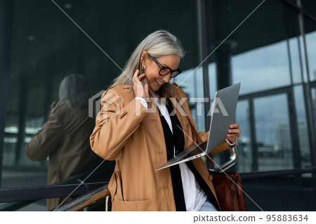 caucasian Middle aged older businesswoman in glasses working on a laptop outside 95883634