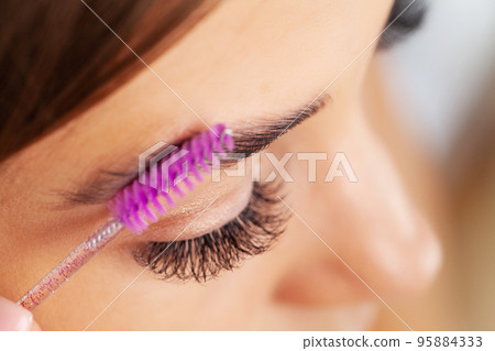 Woman doing morning makeup routine putting mascara in bathroom mirror at home 95884333