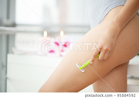 Young woman removing hair on legs with razor at bathroom Young woman removing hair on legs with razor at bathroom 95884592