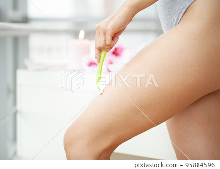 Young woman removing hair on legs with razor at bathroom 95884596