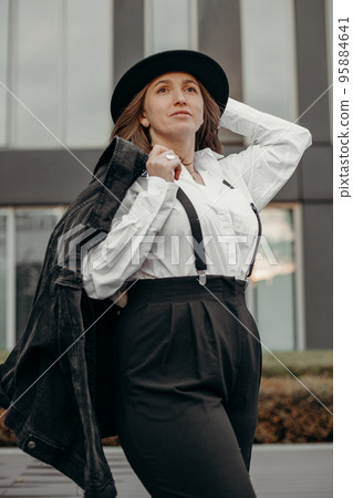 Girl flirt dressed in men's style. Elegant fashionable woman wearing white shirt, black hat. Confident girl posing black suit and hat. 95884641