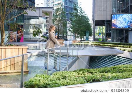 Successful businesswoman in beige suit, standing in city center near sky scrappers and office buildings Successful businesswoman in beige suit, standing in city center near sky scrappers and office buildings 95884809