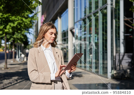 Portrait of corporate woman using her digital tablet, working and walking on street, going to office, multitasking 95884810