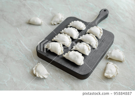 Beautiful raw stuffed dumplings on a wooden cutting board Beautiful raw stuffed dumplings on a wooden cutting board 95884887
