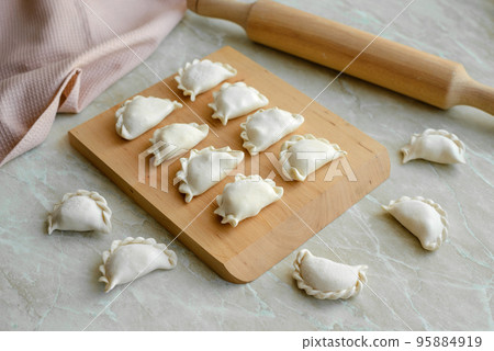 Beautiful raw stuffed dumplings on a wooden cutting board 95884919