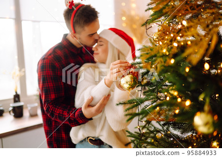 Happy couple decorating christmas tree at home. Smiling Man and Woman together Celebrating Christmas Happy couple decorating christmas tree at home. Smiling Man and Woman together Celebrating Christmas 95884933