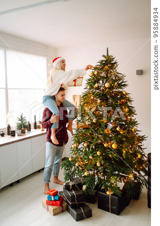 Happy couple decorating christmas tree at home. Smiling Man and Woman together Celebrating Christmas Happy couple decorating christmas tree at home. Smiling Man and Woman together Celebrating Christmas 95884934