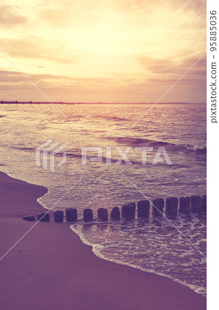 Wooden breakwater at a beach at sunset, selective focus, color toning applied. 95885036