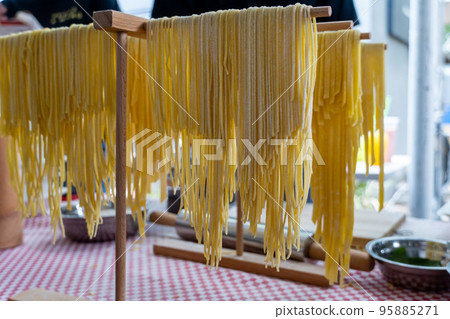 A portrait of freshly made pasta hanging on a pasta dryer 95885271