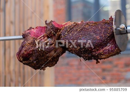 Process of cooking large meat peaces on spit over open fire 95885709