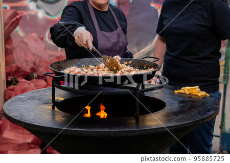 Woman chef cooking paella - fried chicken meat pieces, peppers, peas in huge wok Woman chef cooking paella - fried chicken meat pieces, peppers, peas in huge wok 95885725