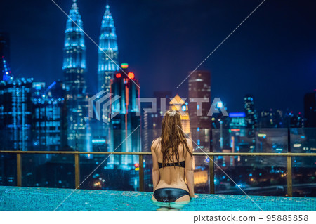 Young woman in outdoor swimming pool with city view at night 95885858