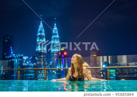 Young woman in outdoor swimming pool with city view at night 95885864