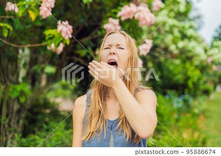 Young woman sneezes in the park against the background of a flowering tree. Allergy to pollen concept Young woman sneezes in the park against the background of a flowering tree. Allergy to pollen concept 95886674