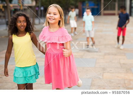 Happy blonde preteen girl walking with african american girl playmate 95887056