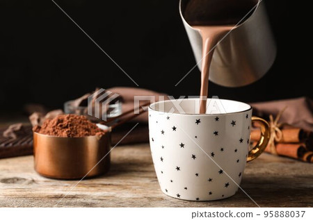 Pouring hot cocoa drink into cup on wooden table Pouring hot cocoa drink into cup on wooden table 95888037