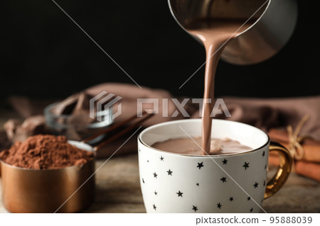 Pouring hot cocoa drink into cup on wooden table Pouring hot cocoa drink into cup on wooden table 95888039