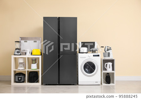 Modern refrigerator and other household appliances near beige wall indoors Modern refrigerator and other household appliances near beige wall indoors 95888245