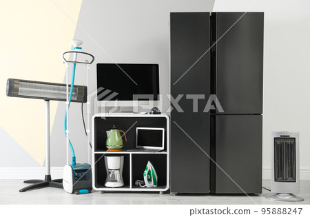 Modern refrigerator and other household appliances near color wall indoors 95888247