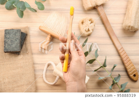 Woman holding natural bamboo toothbrush over table with bath items, top view Woman holding natural bamboo toothbrush over table with bath items, top view 95888319