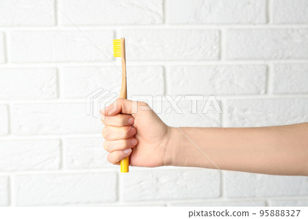 Woman holding bamboo toothbrush against white brick wall, closeup Woman holding bamboo toothbrush against white brick wall, closeup 95888327