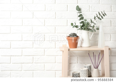 Beautiful plants and accessories on wooden shelves near brick wall at home. Space for text 95888384