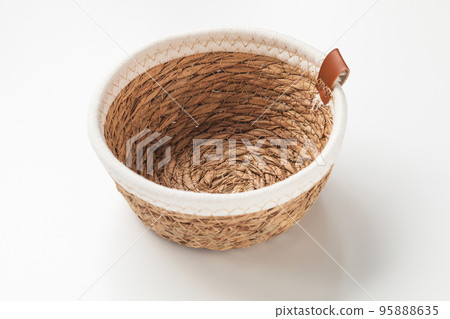 Small round seagrass and cream white cotton rope storage basket with rim. Trendy natural multifunctional table container for fruits and hobbies. Close up, copy space 95888635
