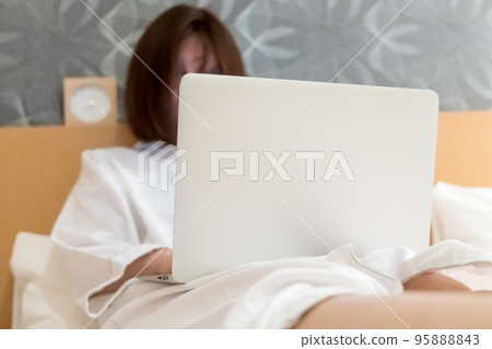 Woman operating a computer on the bed Remote work image Woman operating a computer on the bed Remote work image 95888843