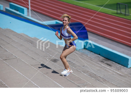 Young caucasian woman running on stadium stairs outdoors.  95889003