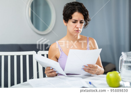 Frustrated brunette woman is unhappy with payment document for utilities Frustrated brunette woman is unhappy with payment document for utilities 95889830